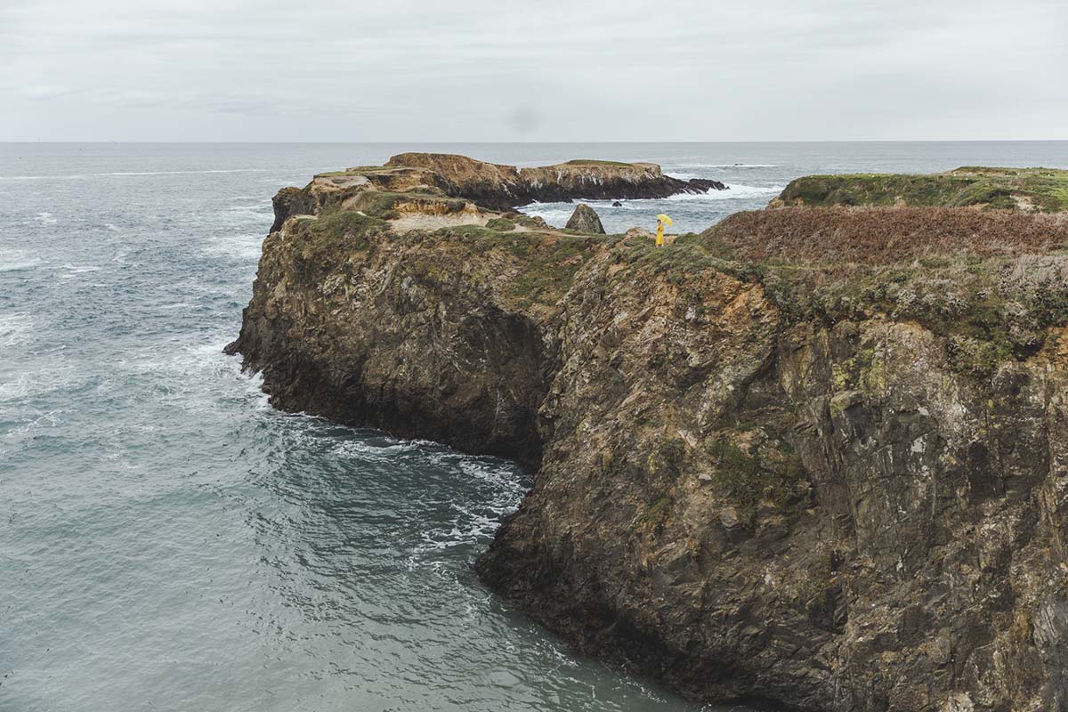 Girl in a Yellow Rain Jacket with Yellow Umbrella Standing on Cliff Over the Ocean